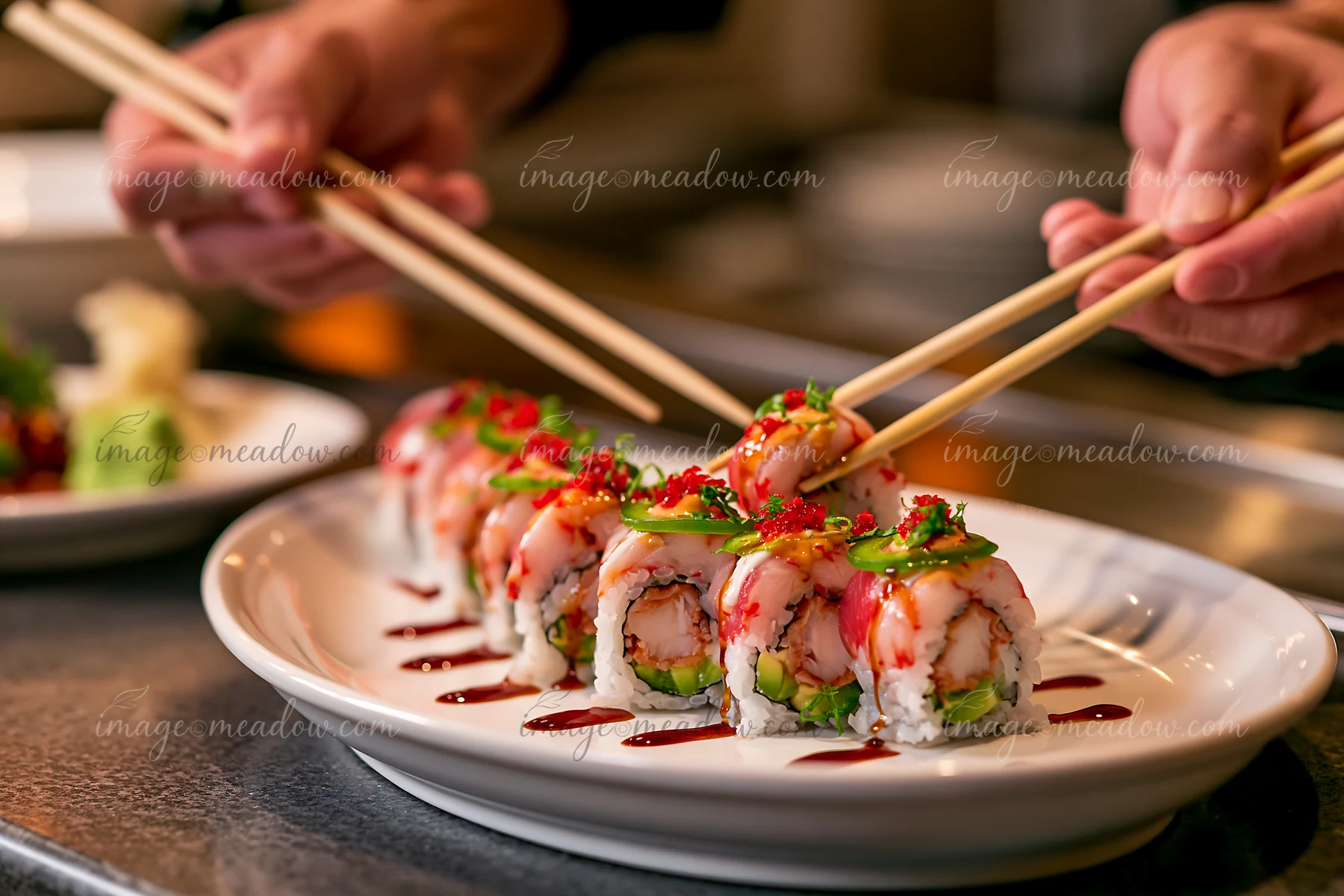 Sushi chef uses chopsticks to pick up a dragon roll close-up on a white plate.