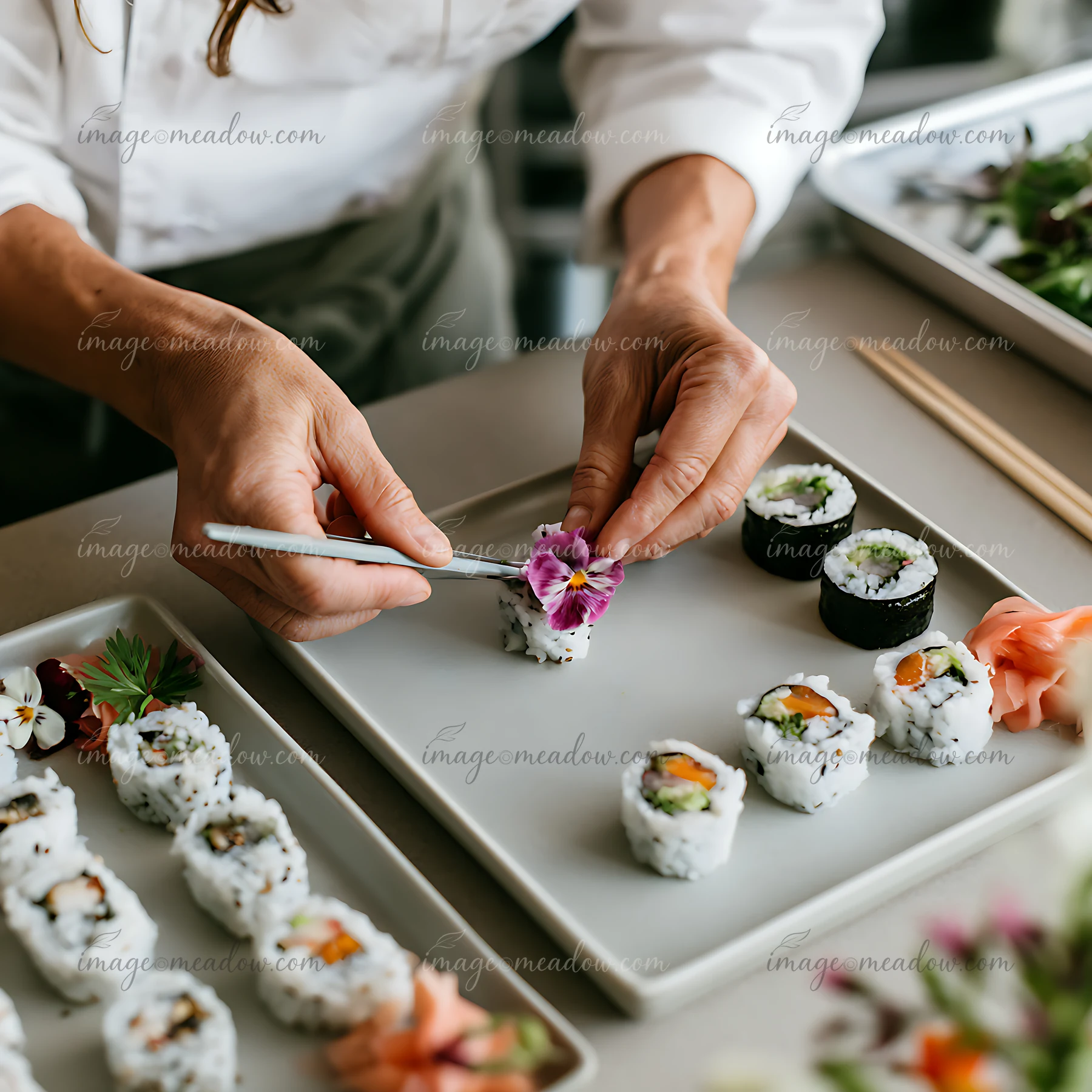 Sushi chef uses tweezers to place a purple edible flower on a plate of sushi rolls.