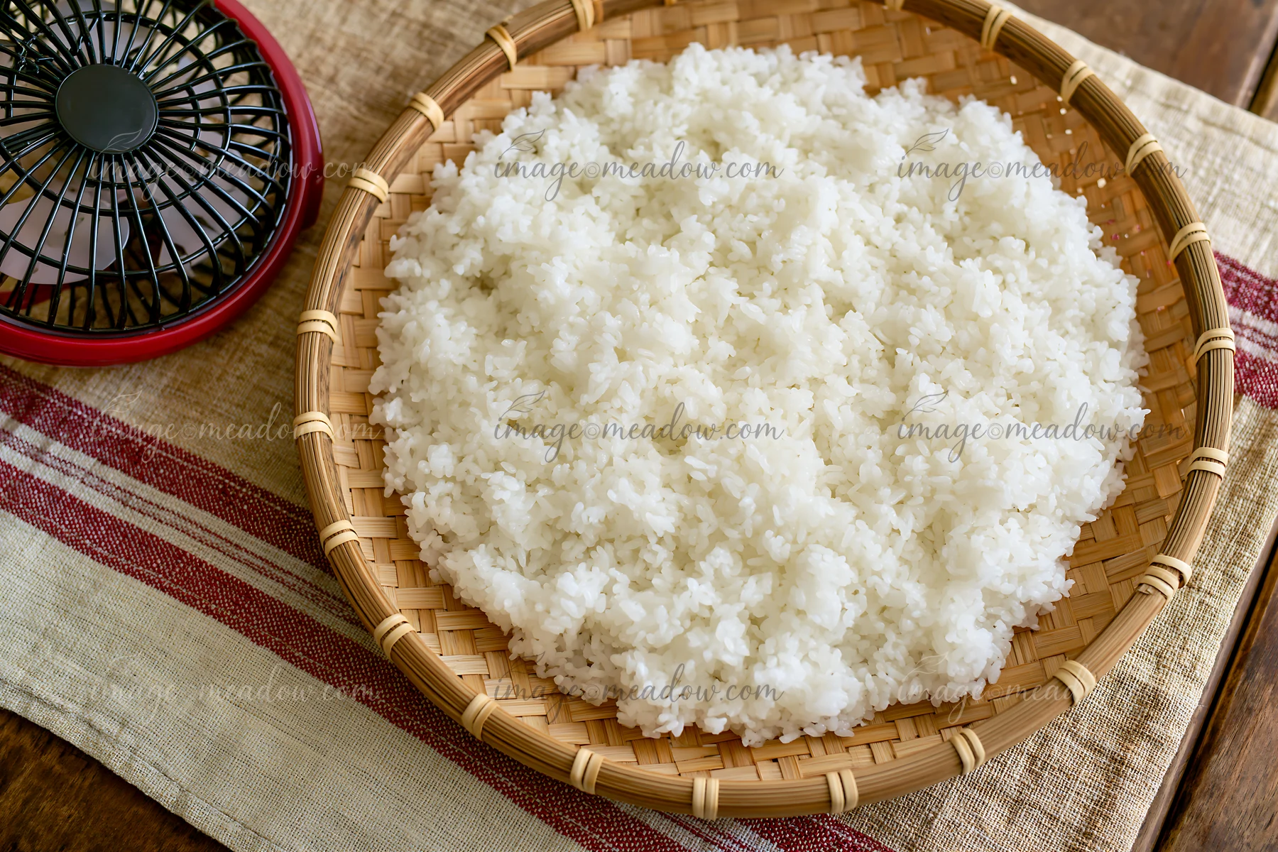 Sushi rice cooling on a bamboo tray sits on a table.
