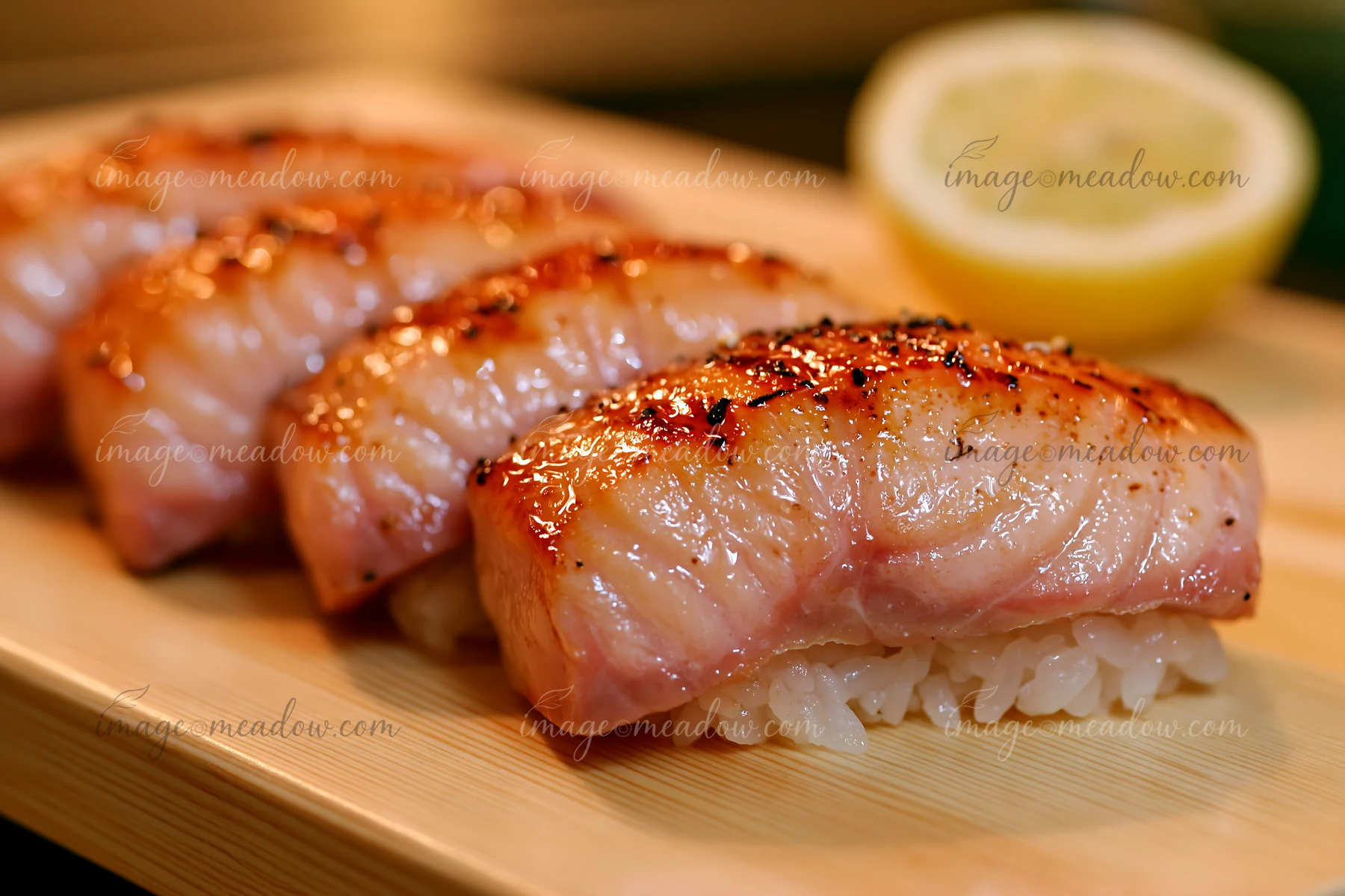 Sushi with lemon garnish close-up showcases beautifully grilled pieces of fish over sushi rice, served on a bamboo plate.