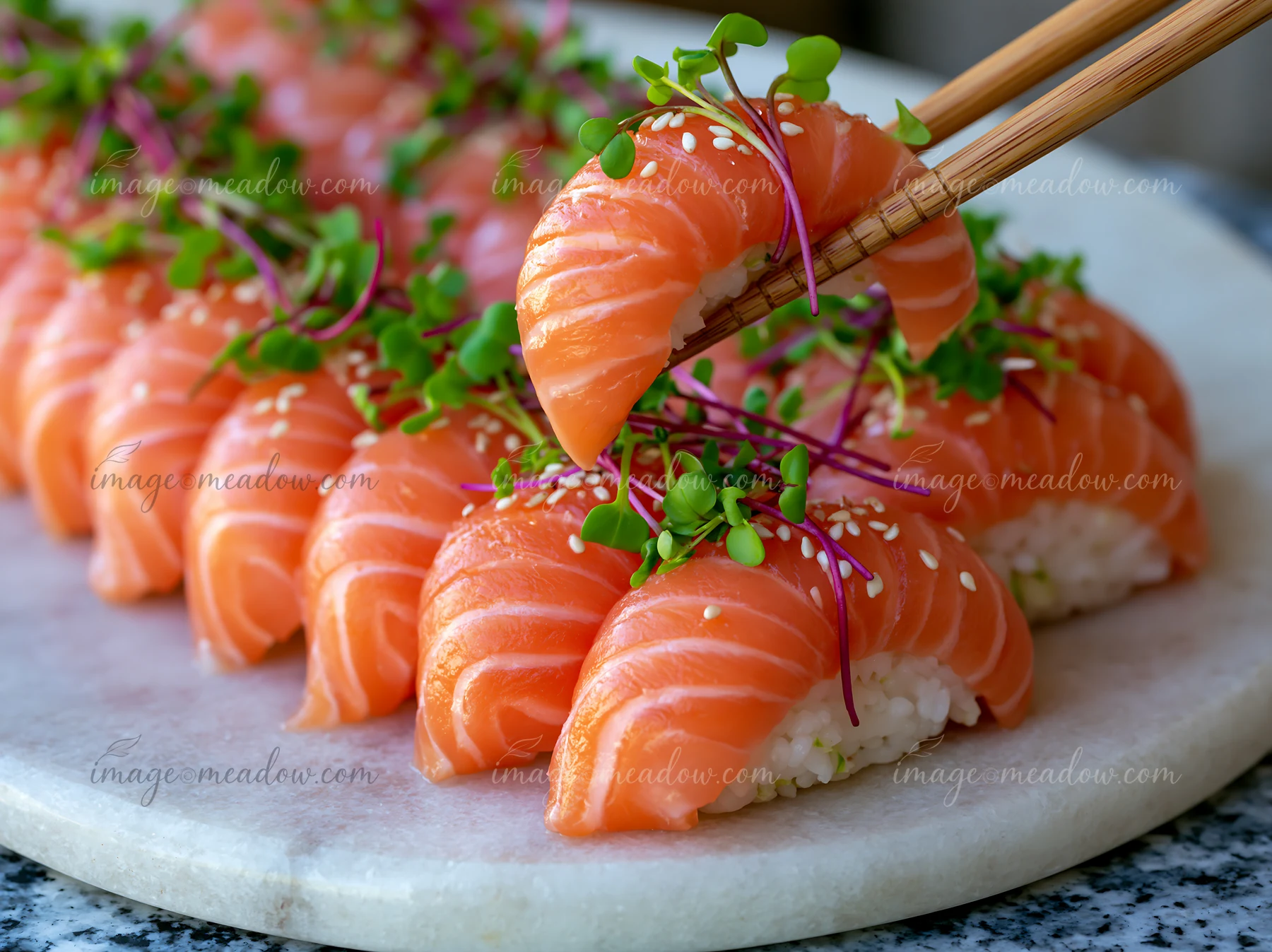 Sushi with microgreens close-up shows a hand using chopsticks to pick up sushi topped with salmon and garnished with microgreens and sesame seeds on a marble pl