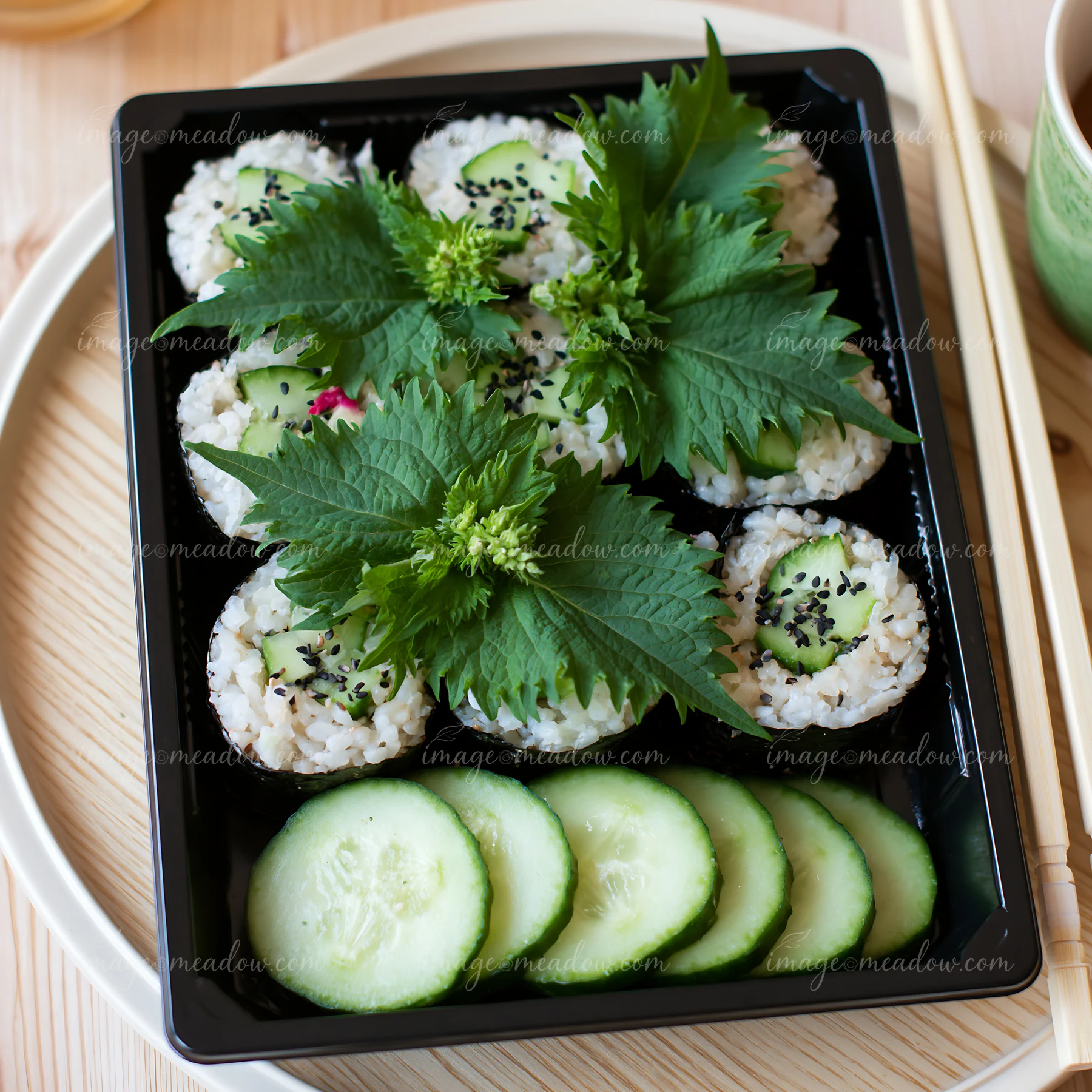 Sushi with shiso leaves is arranged neatly in a black tray with cucumber slices.