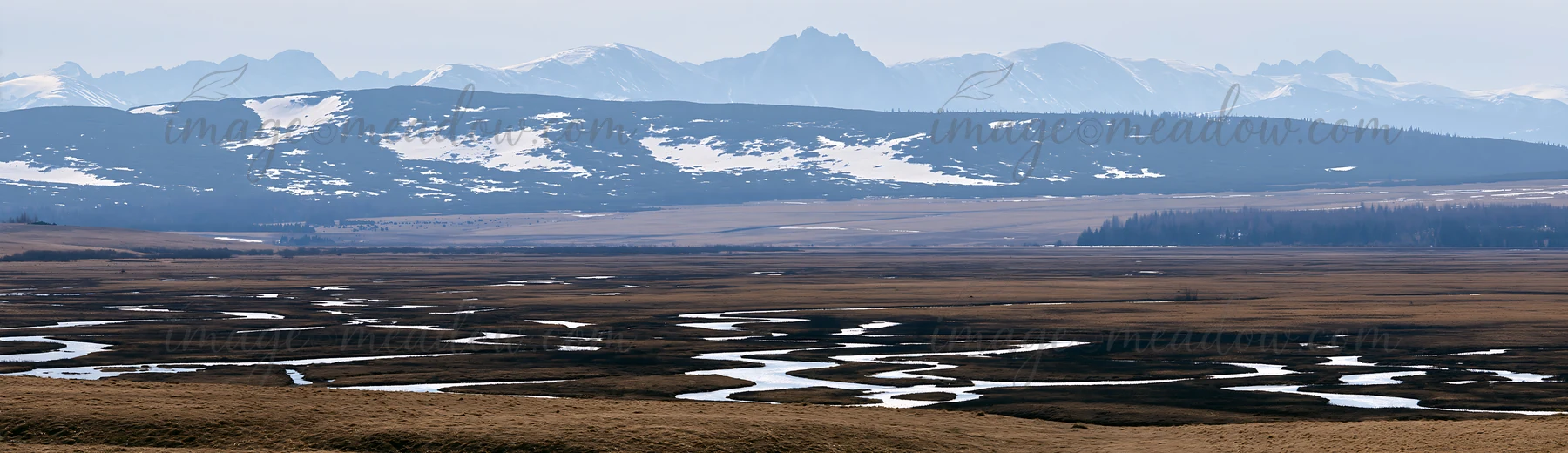 Winding streams flow through a meadow in the Tatra mountains during spring. Snow-melt creates puddles and gives life to the landscape. The mountains stand in th