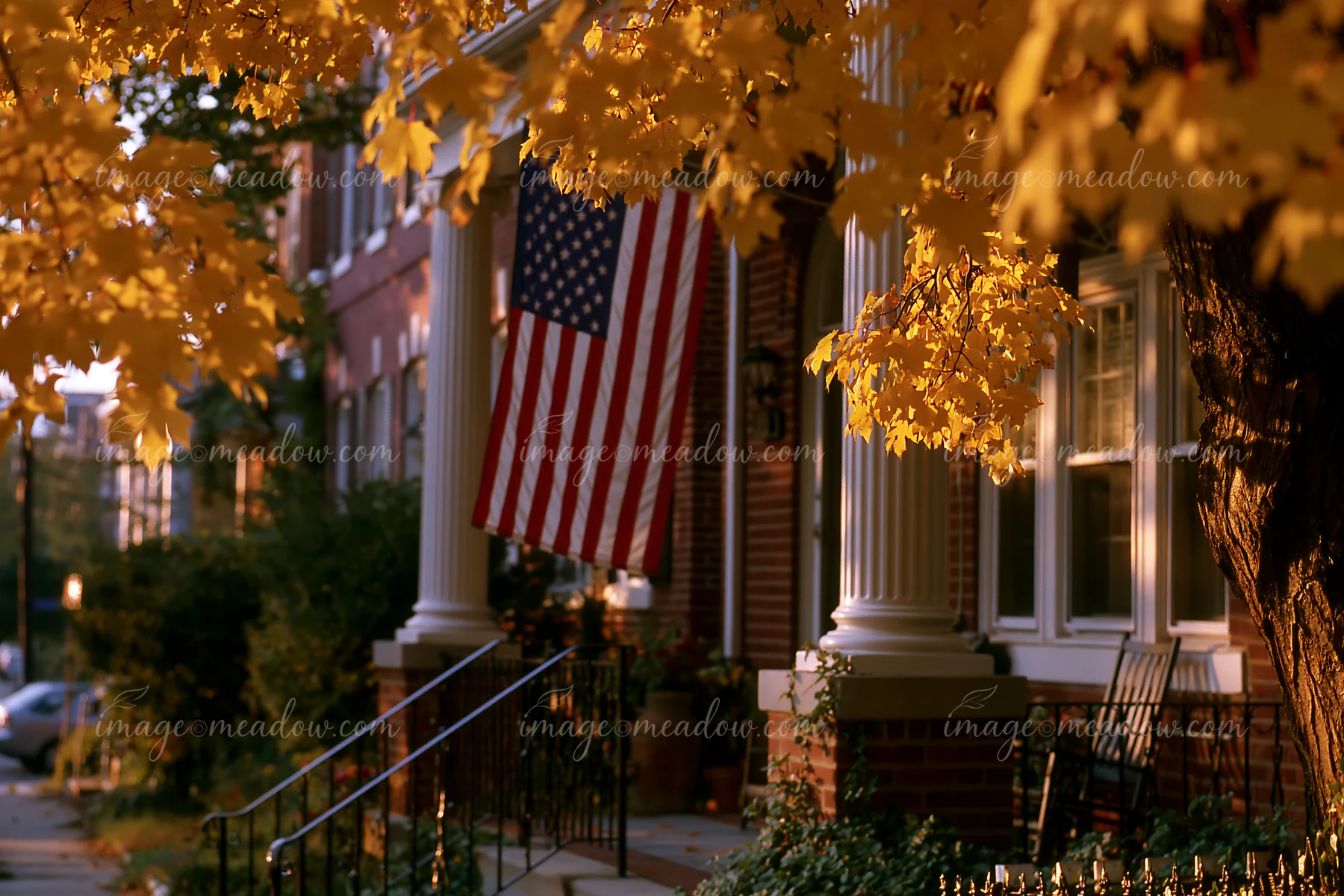 The American flag hanging from the porch adds character to the home, surrounded by vibrant autumn leaves.