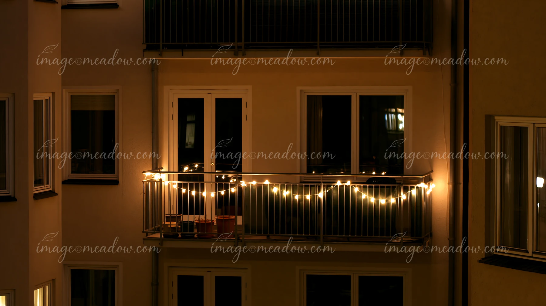 The balcony of a residential building features warm white Christmas lights glowing softly against the dark night sky.