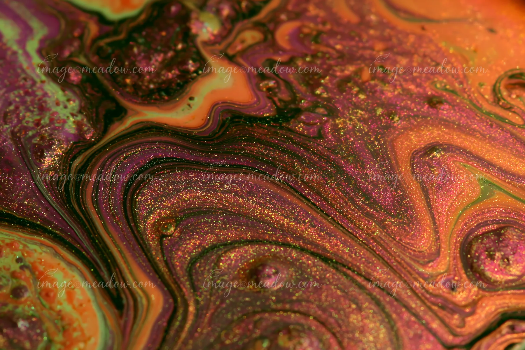 The photograph shows a colorful abstract swirl glittering pattern featuring vibrant hues and shimmering effects on a smooth surface.