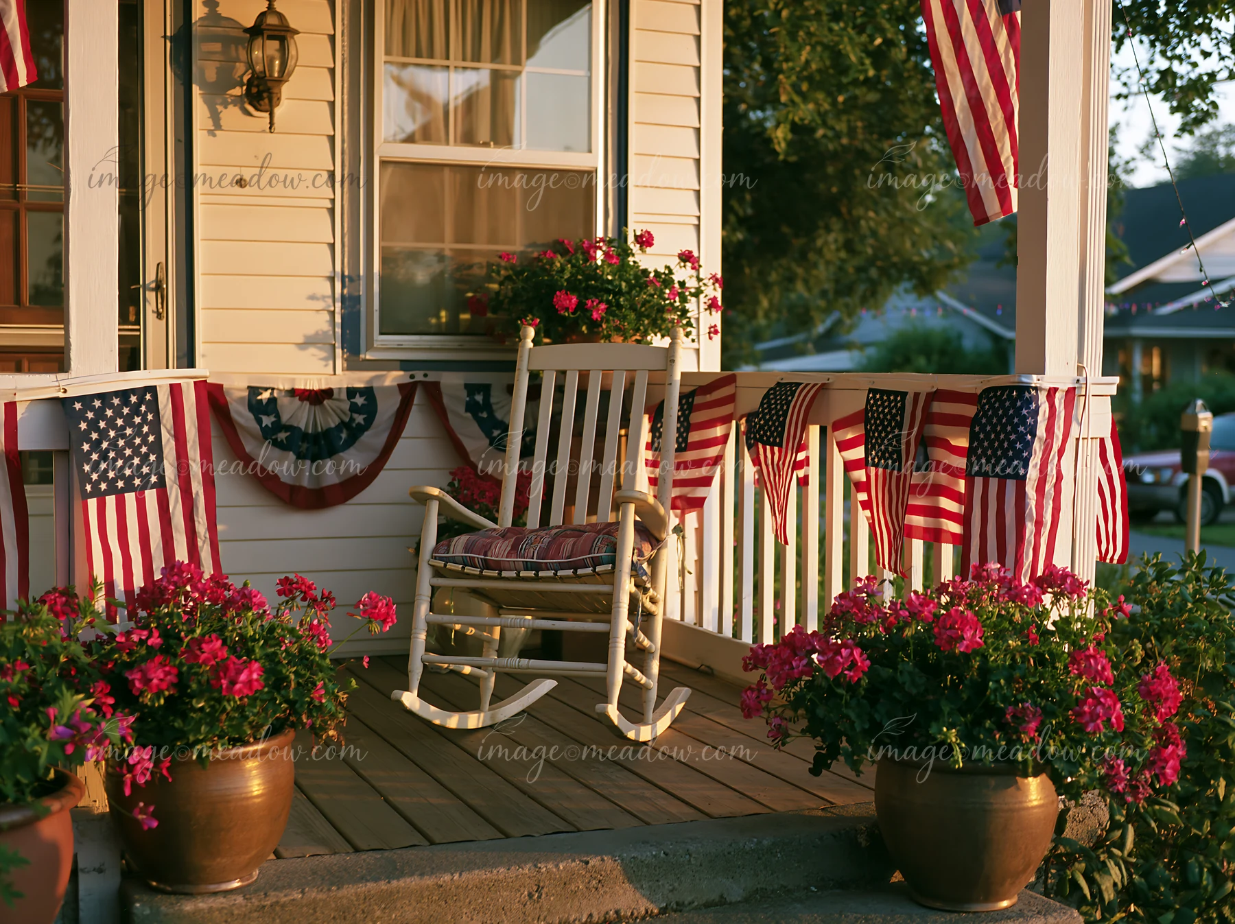 The porch features American flag decorations, planters with flowers, and a rocking chair.