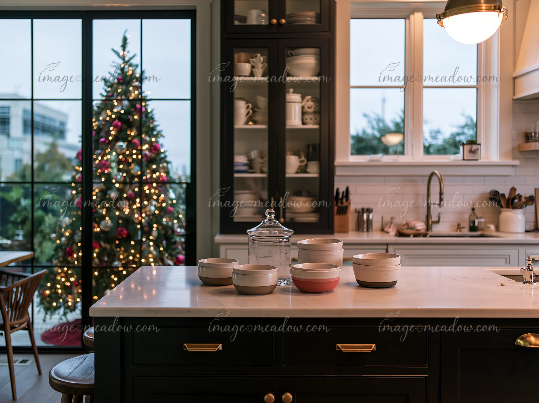 This kitchen features a marble countertop with various bowls and a large Christmas tree visible through a window.