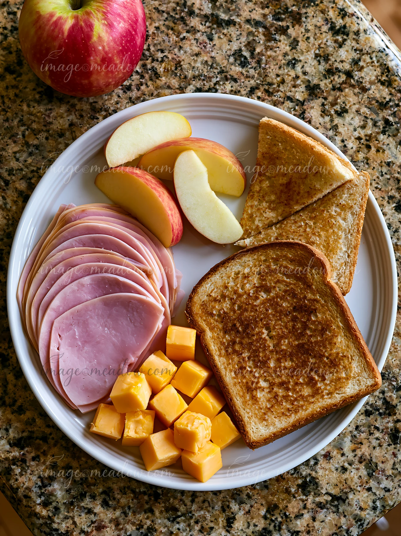 This plate features cold cuts, cheese cubes, sliced apples, and toast.