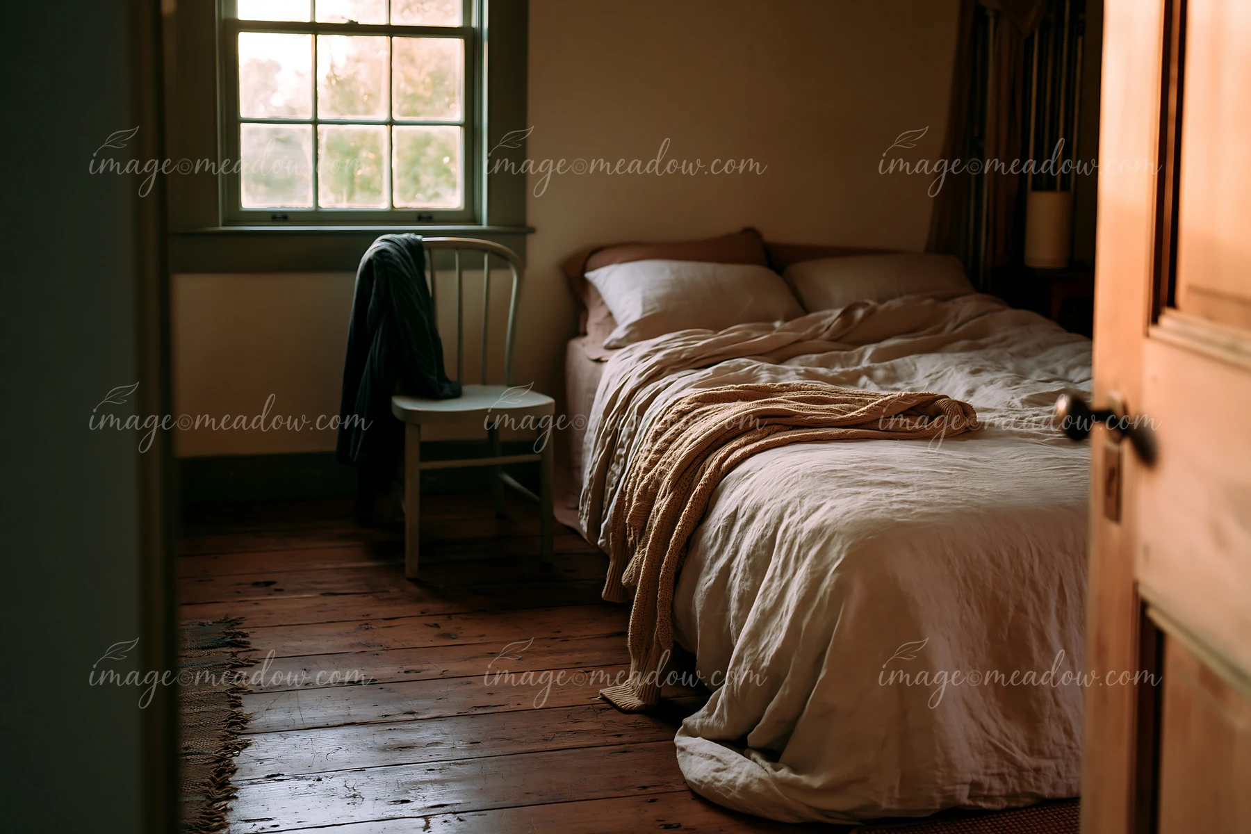 This rustic bedroom showcases a bed with linen bedding, a chair, and wooden floors.