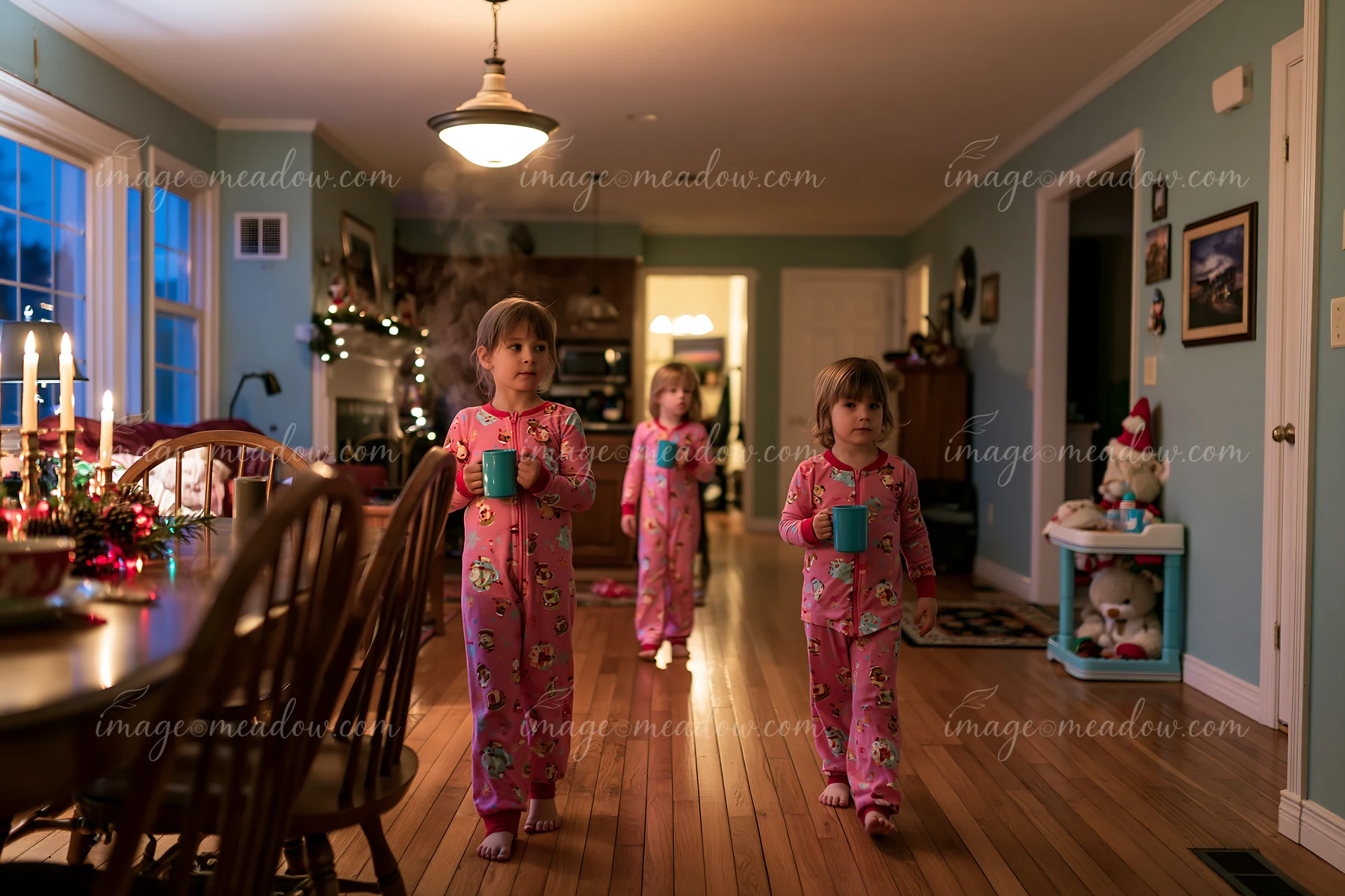 Three children wearing matching pajamas walk through a cozy living room while holding mugs.