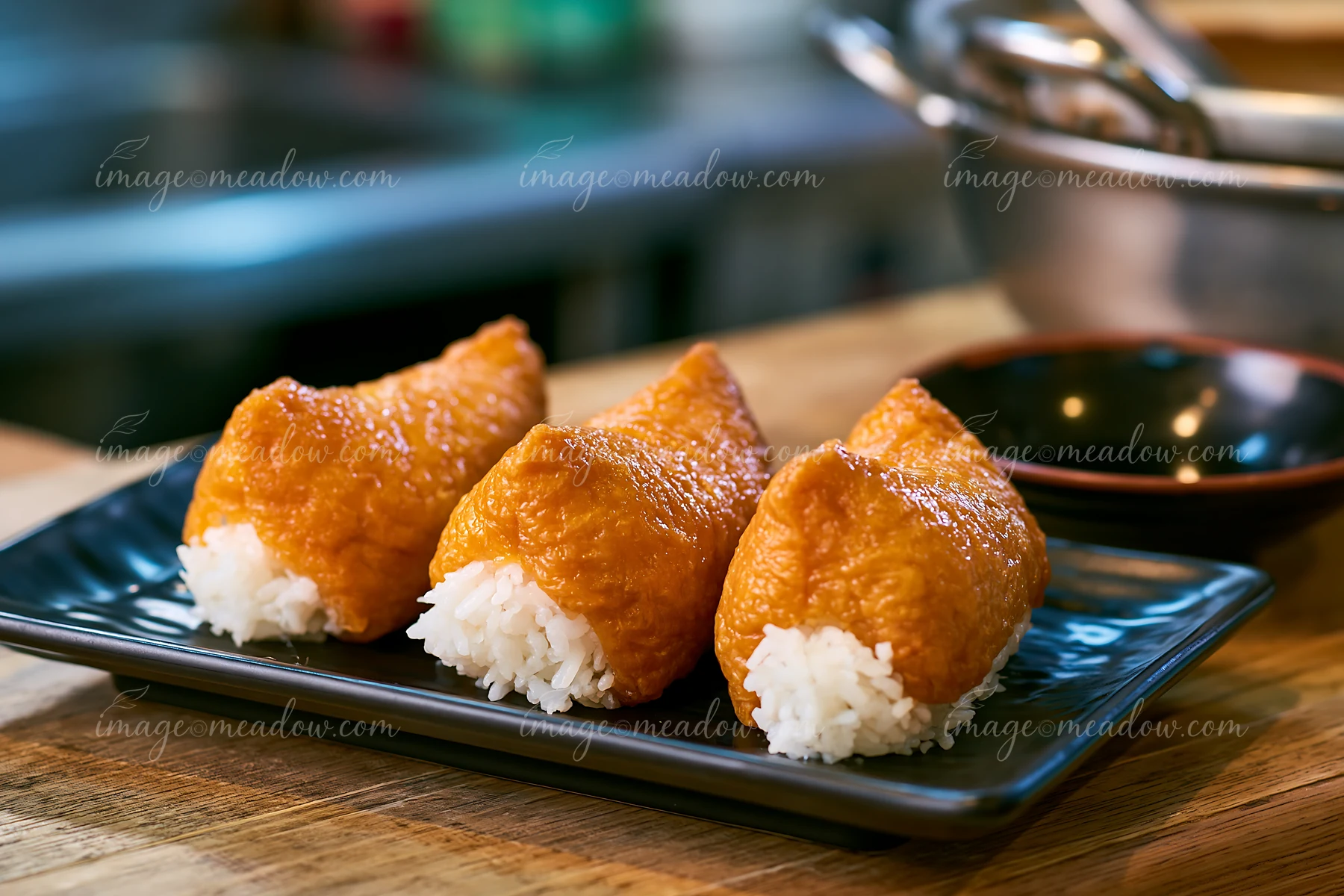 Three inari sushi pockets filled with rice are placed on a black plate.