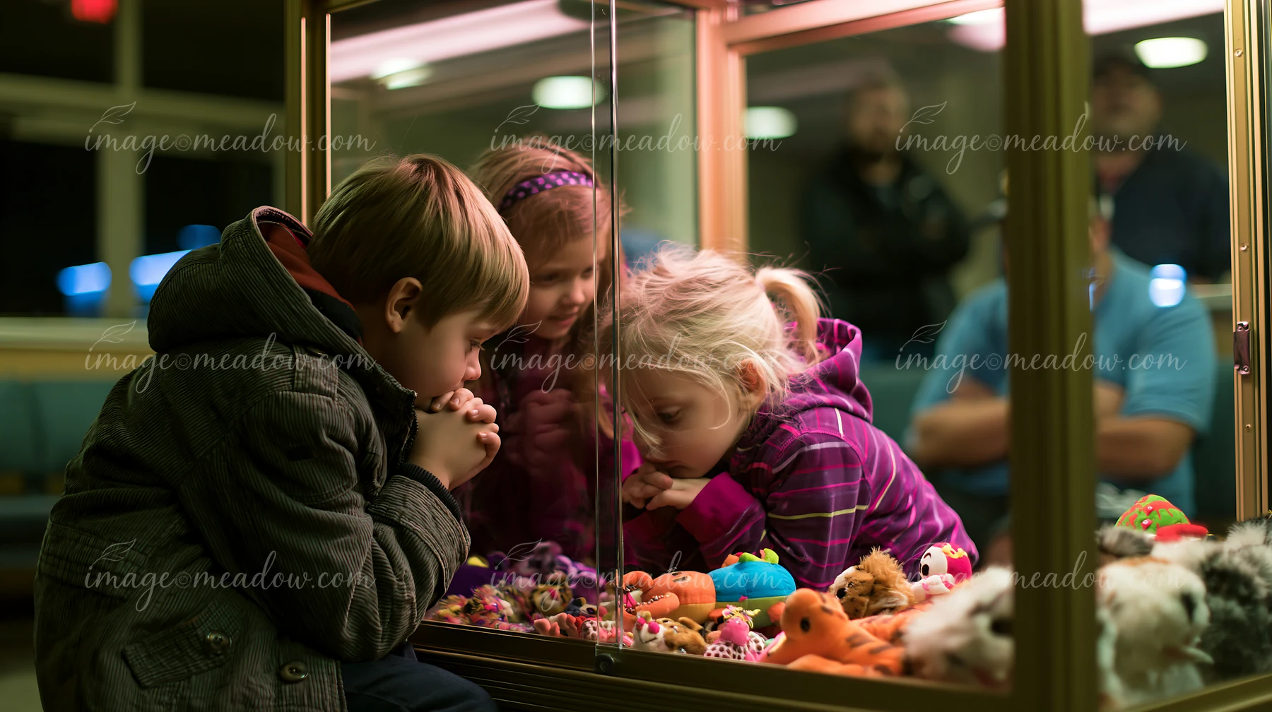 Three siblings play a claw-style prize game, focused on the colorful toys inside the glass display.
