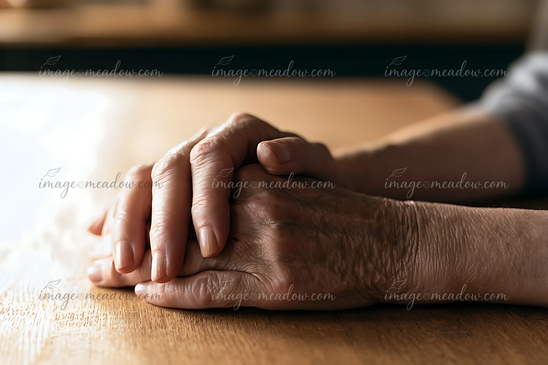Two hands are intertwined and resting on a wooden table in warm, soft light.