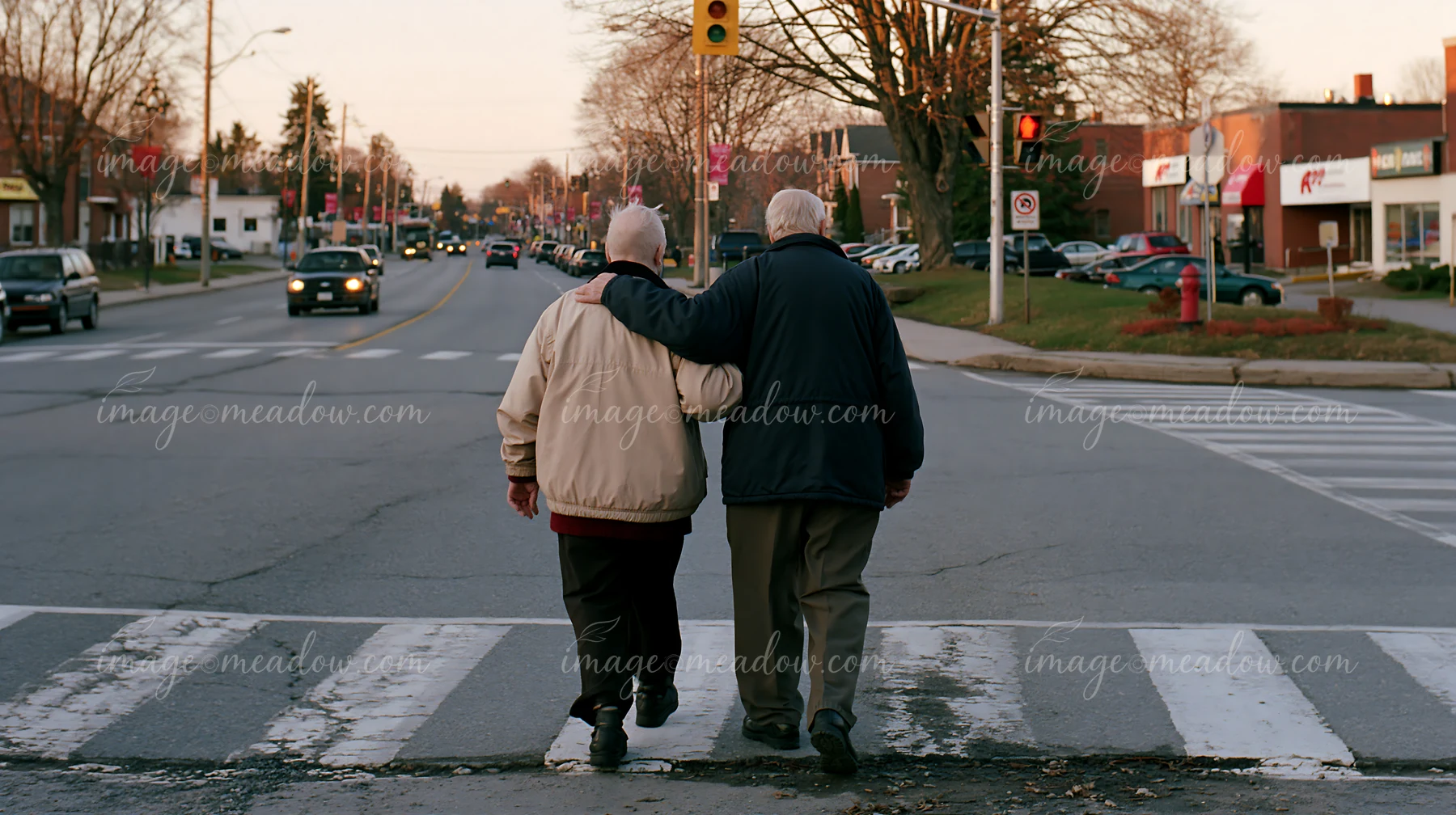 Two individuals are crossing a street, with one person providing support to another.