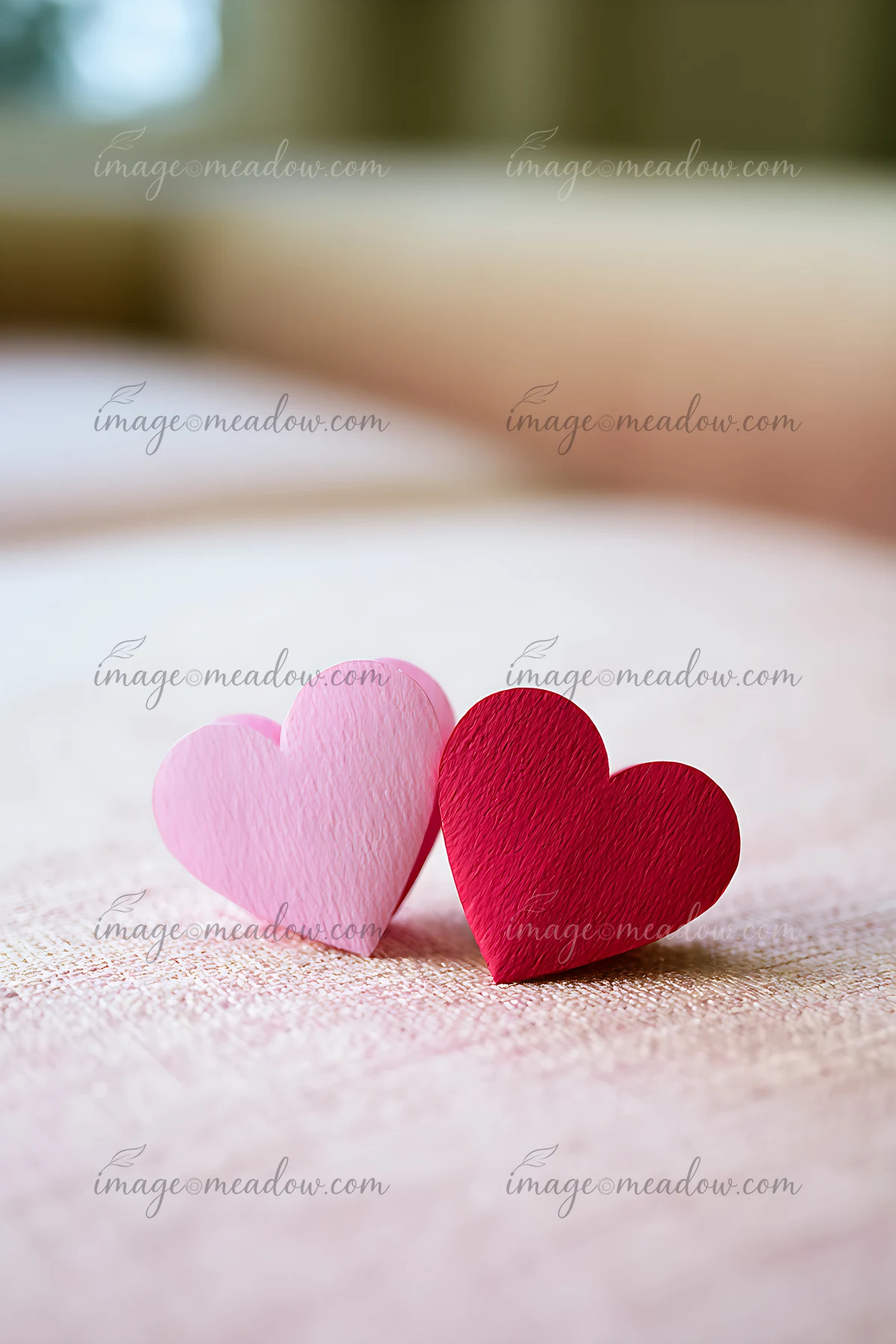 Two paper hearts, one pink and one red, rest on a soft fabric surface.