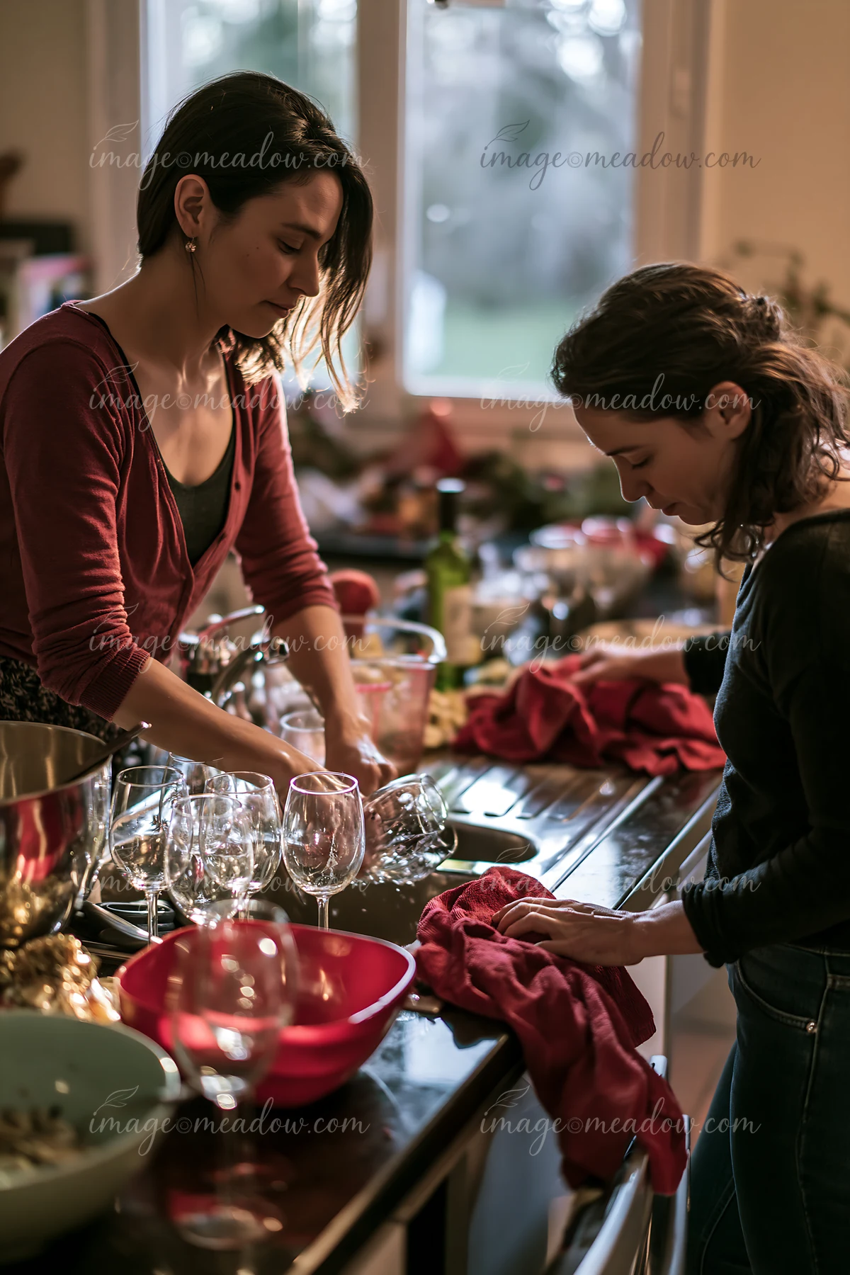 Two women are cleaning up the kitchen after a holiday gathering, washing dishes and wiping down surfaces.