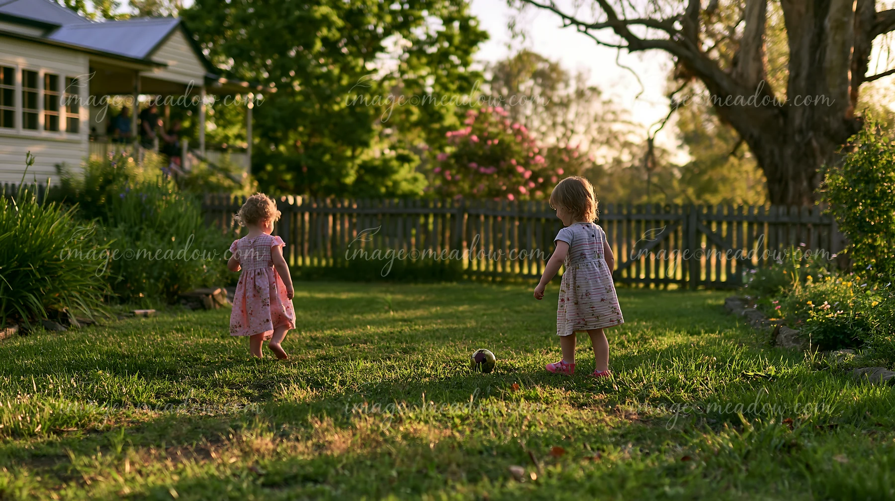 Two young children play in a green farmhouse garden as the sun sets.