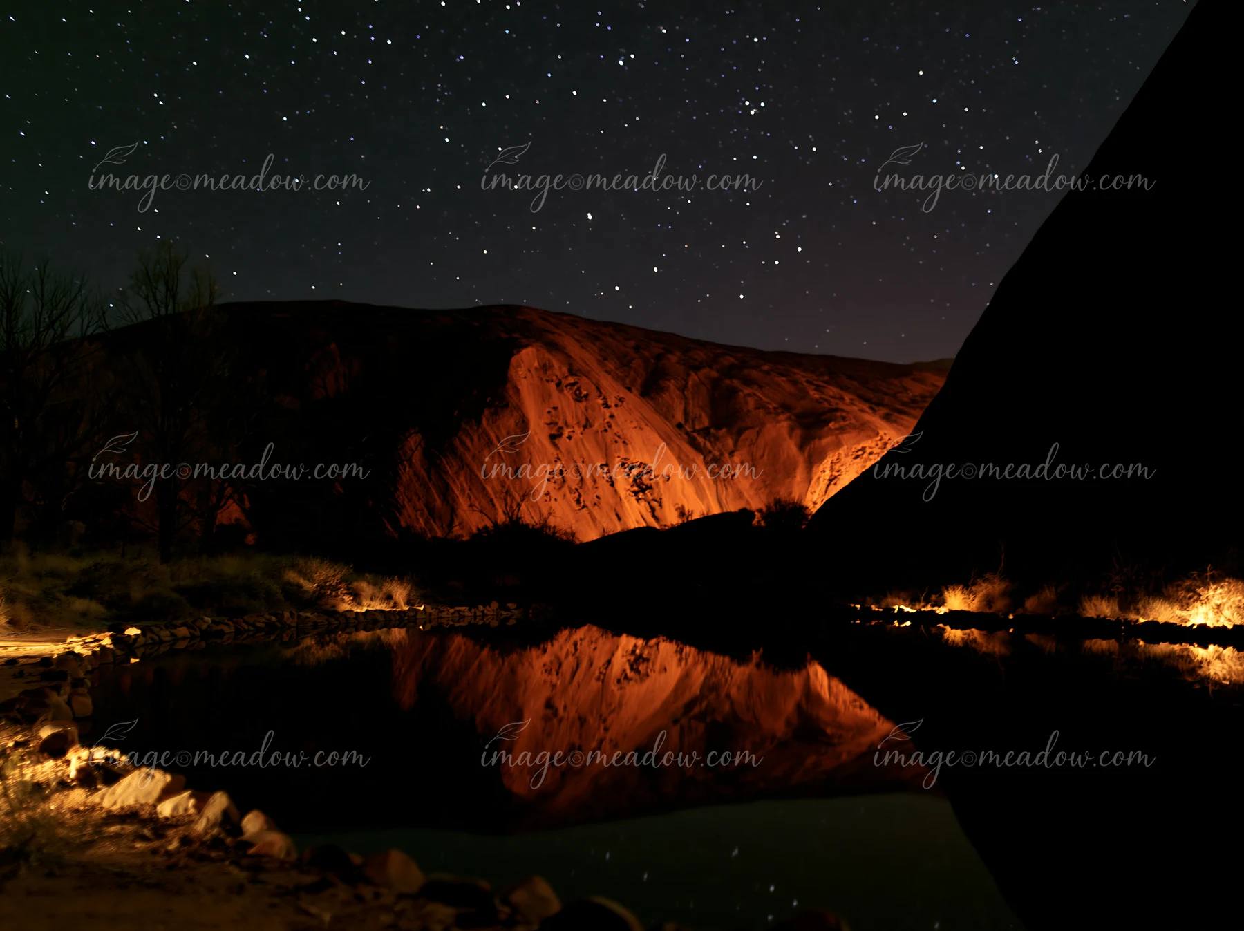 Uluru under a starry night sky shows the famous rock formation illuminated by natural light.