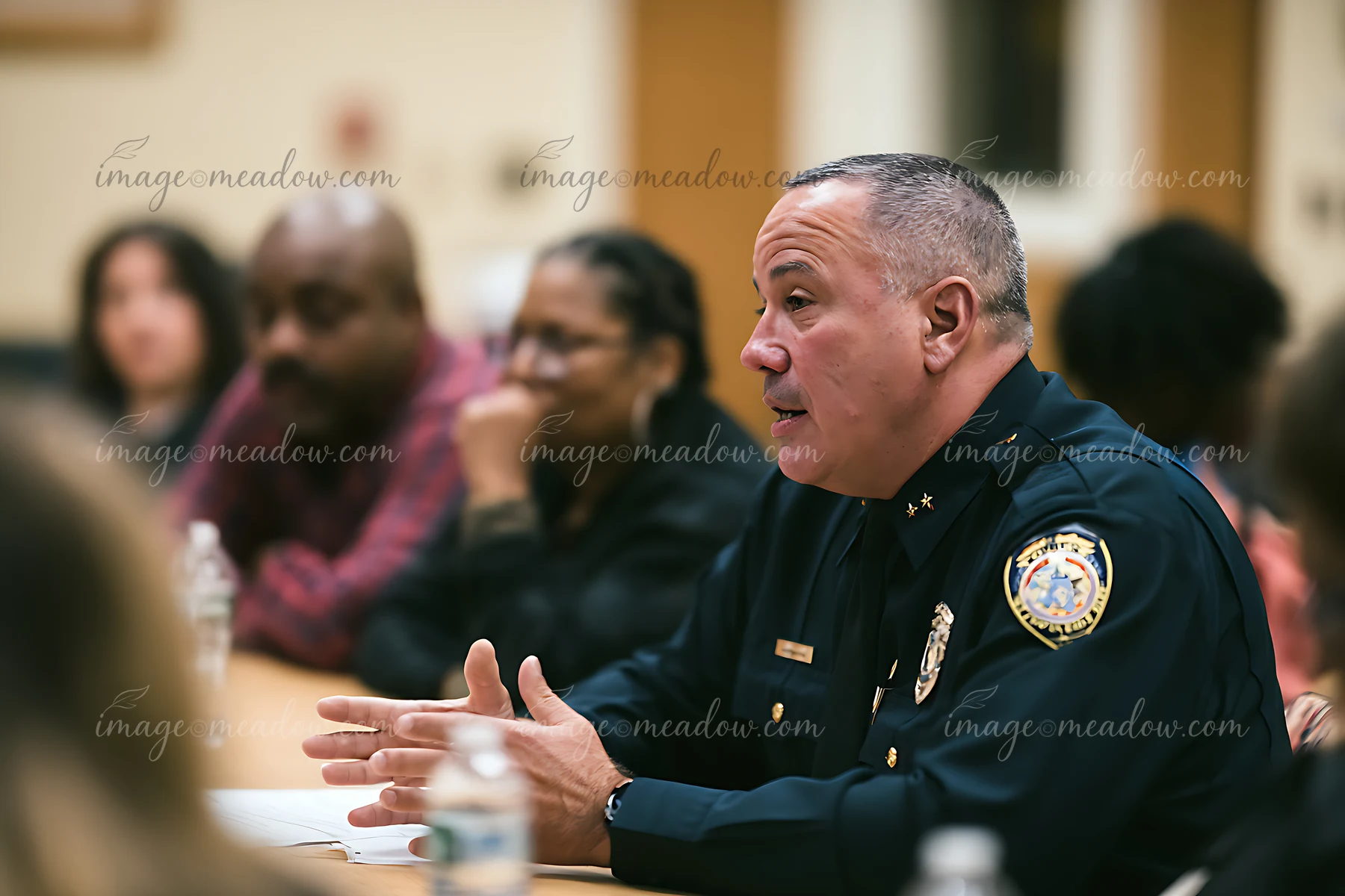 Uniformed police chief speaks at a table during a civilian oversight meeting with community members.