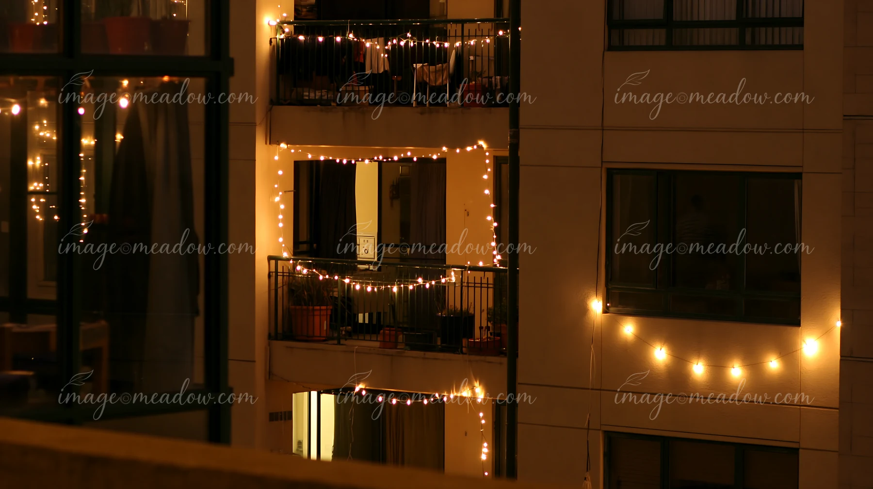 Warm Christmas lights decorate balconies and windows on a residential apartment building at night.