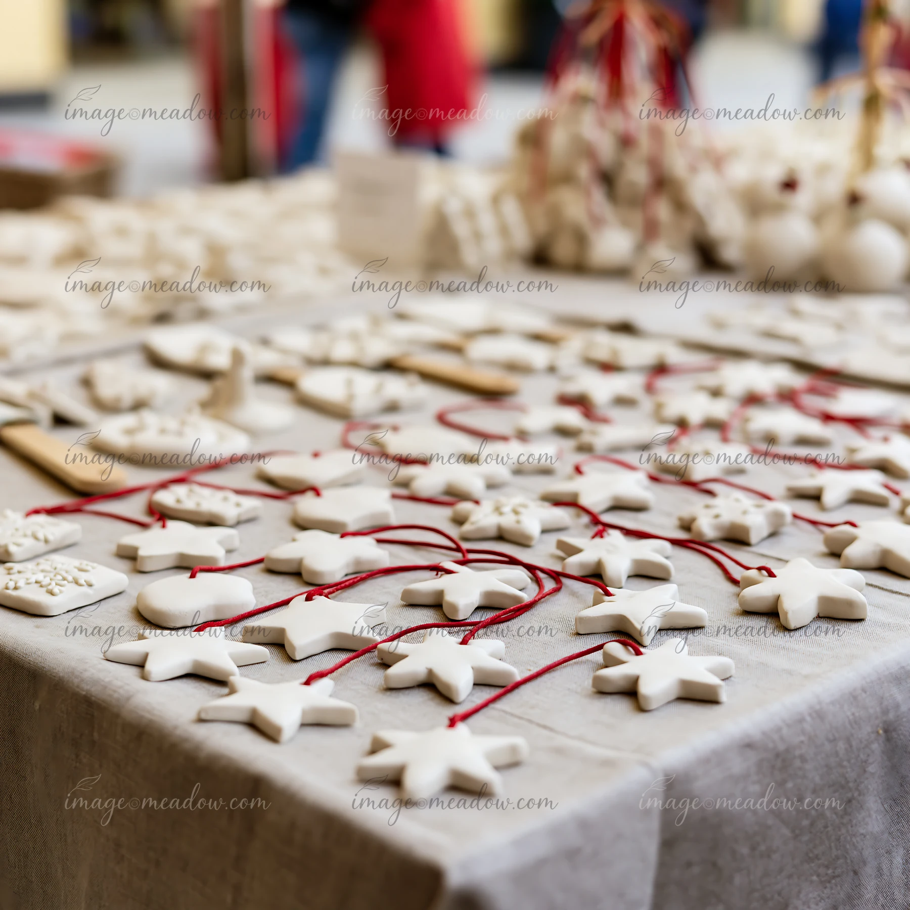 White handmade star ornaments with red cords displayed on a fabric-covered Christmas market stall table.