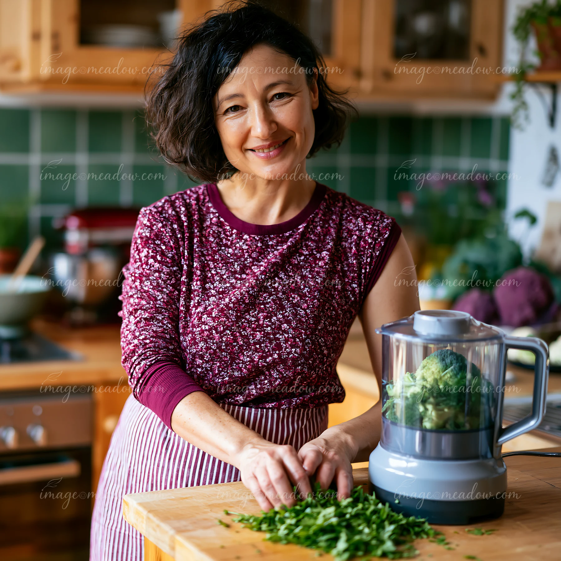 Woman preparing chopped herbs beside a food processor on a kitchen counter.