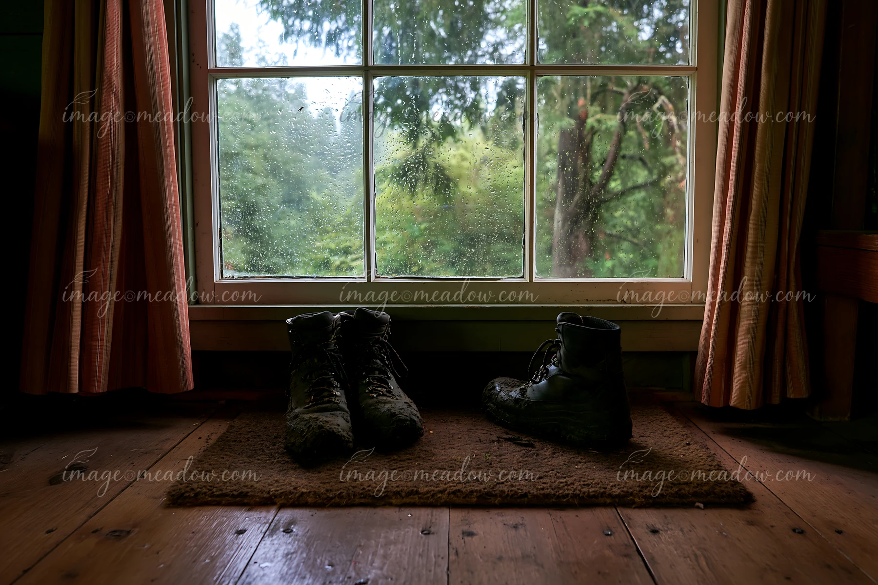 Worn boots sit on a mat inside a cabin near a window.