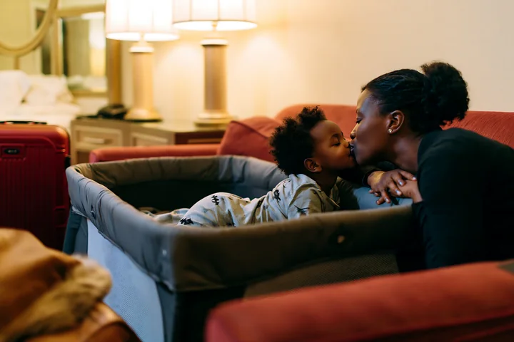 A child kisses a parent at bedtime in a cozy hotel room, showing their bond.