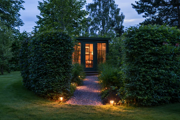 A garden studio stands illuminated at dusk with soft lighting along the pathway.