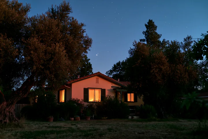 A house under stars during blue hour is visible with warm light shining from the windows.