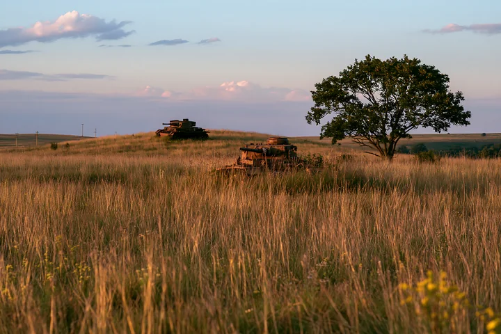 A panzer tank surrounded by grass sits on a hill under a clear sky.