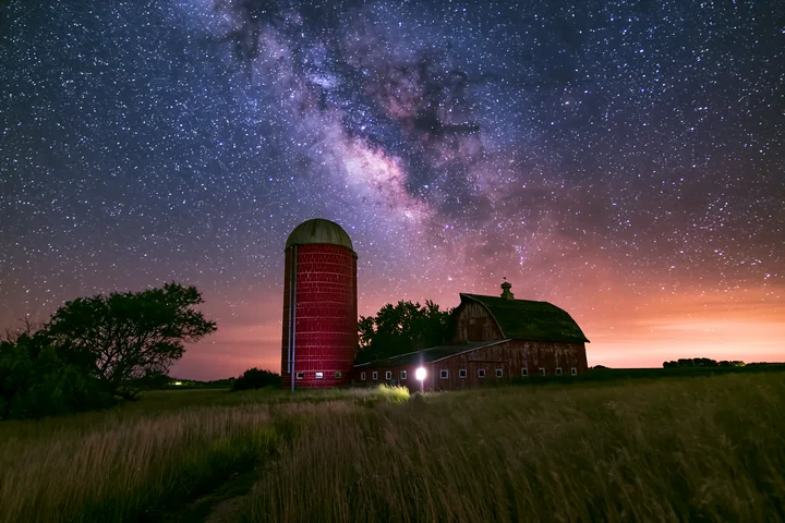 A rural scene shows a red silo and barn under a starry night sky.