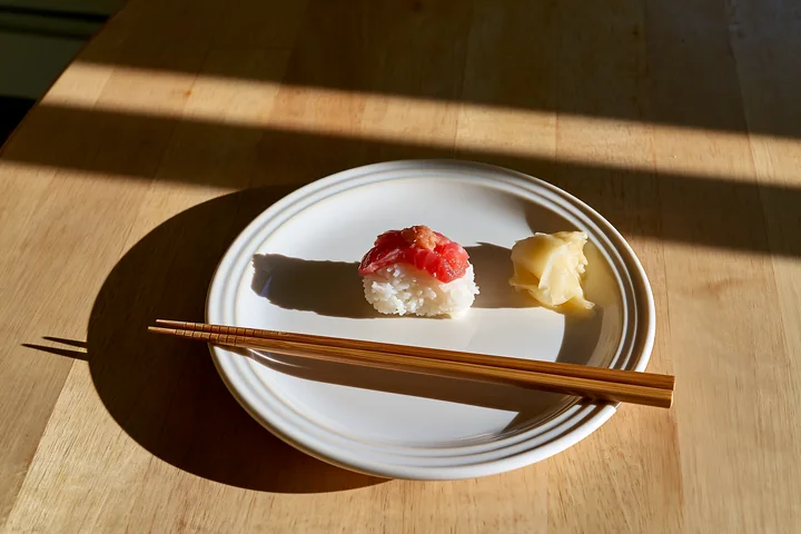 A single piece of sushi sits on a white plate with pickled ginger alongside.