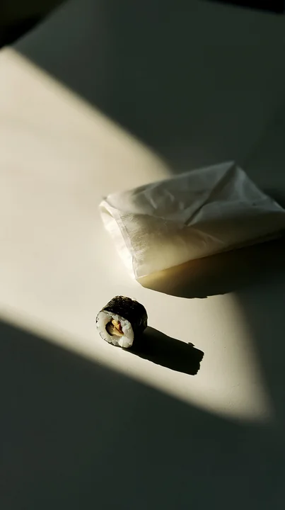A single sushi piece on a contemporary dining table rests beside a folded napkin.