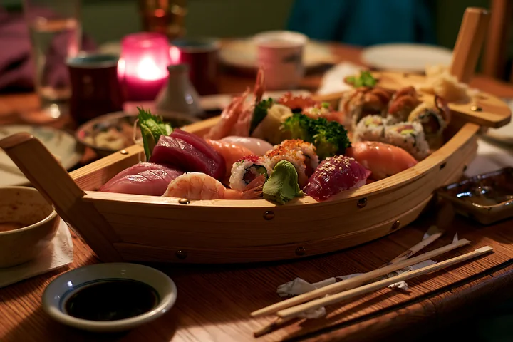 A wooden boat holds a variety of sushi including nigiri and rolls, placed on a table in a restaurant.