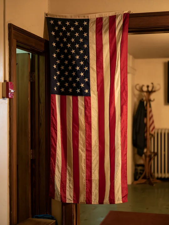 An American flag hanging vertically is displayed inside a room with wooden features.