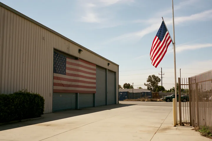 An American flag waves outside a factory where another large flag is displayed on the wall.