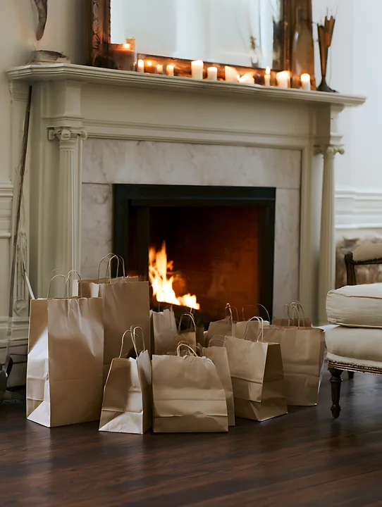 Brown shopping bags are placed beside a warm fireplace in a living room.