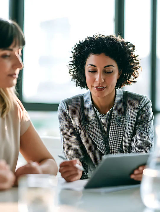 Businesswoman uses a tablet at a table with a colleague in a bright meeting room.