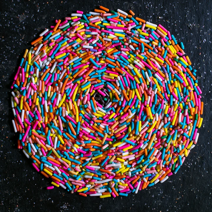 Rainbow sprinkles arranged in a swirl create a colorful design on a dark surface.