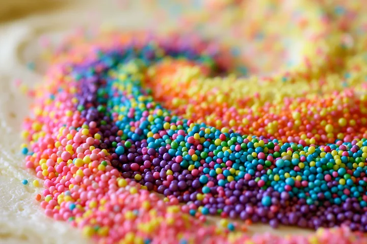 Rainbow sprinkles arranged in a swirl create a colorful pattern on a dessert surface.