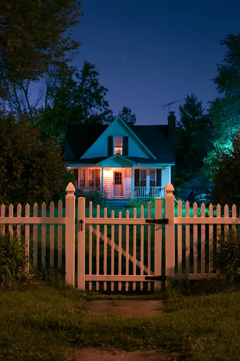 The image features a country home with a white fence illuminated at night under a clear sky.