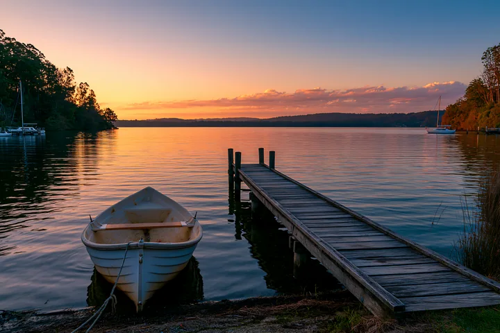 A boat sits at a wooden dock on a coastline with sheltered bay as the sun sets.