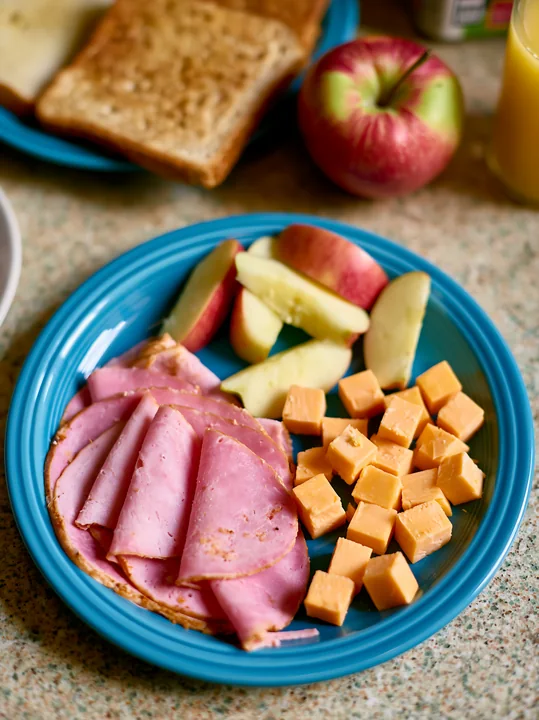 A breakfast plate with cold cuts, cheese, and fresh apple slices is set on a kitchen counter.