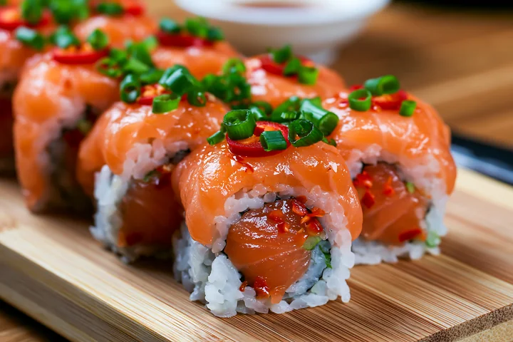 A close-up view of a spicy salmon sushi roll with chili on a wooden board.