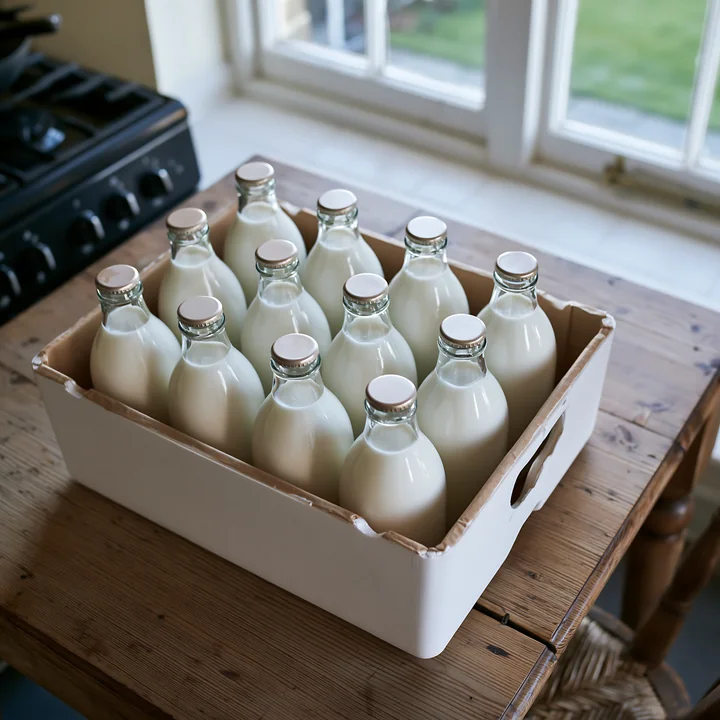 A collection of milk bottles is arranged in an insulated delivery box on a wooden table.
