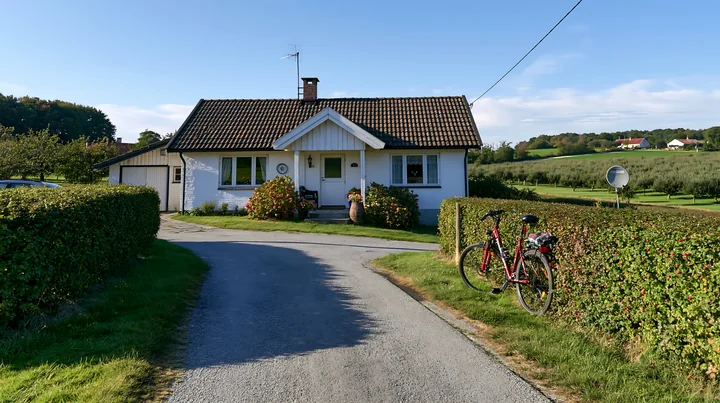 A country home with bicycle outside sits on a quiet road with a grassy lawn and hedges.