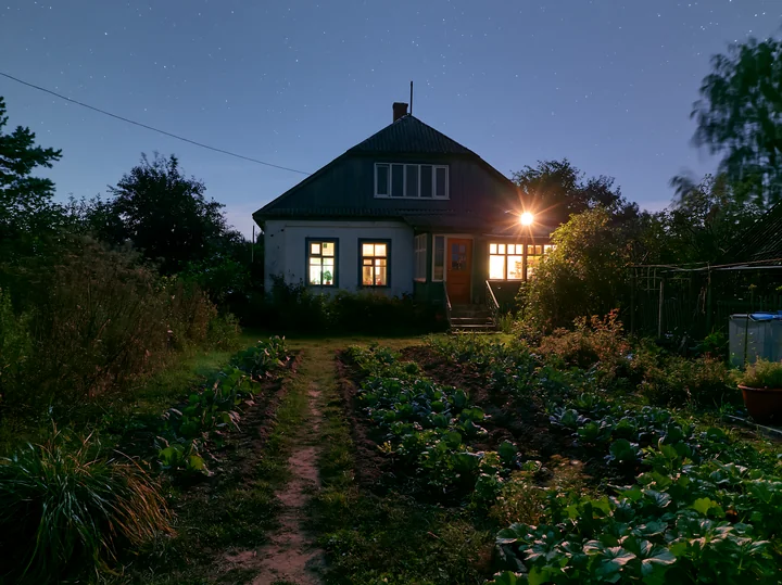 A country house is visible at night with warm lights glowing from the windows.