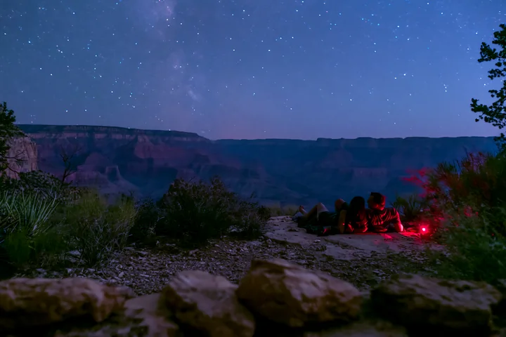 A couple is stargazing in a national park, lying on the ground while observing the night sky filled with stars.